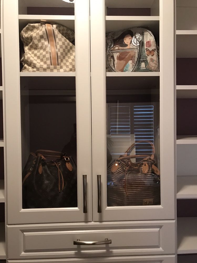 A closet with glass doors and shelves filled with handbags.