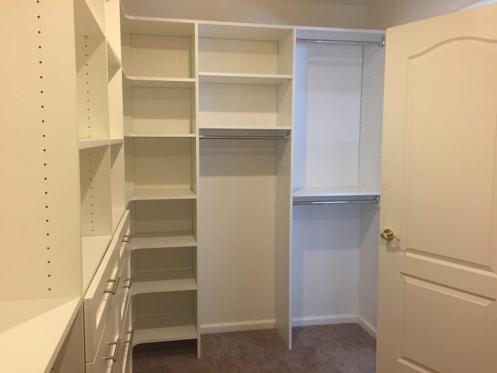 A walk in closet with white shelves and drawers and a door.