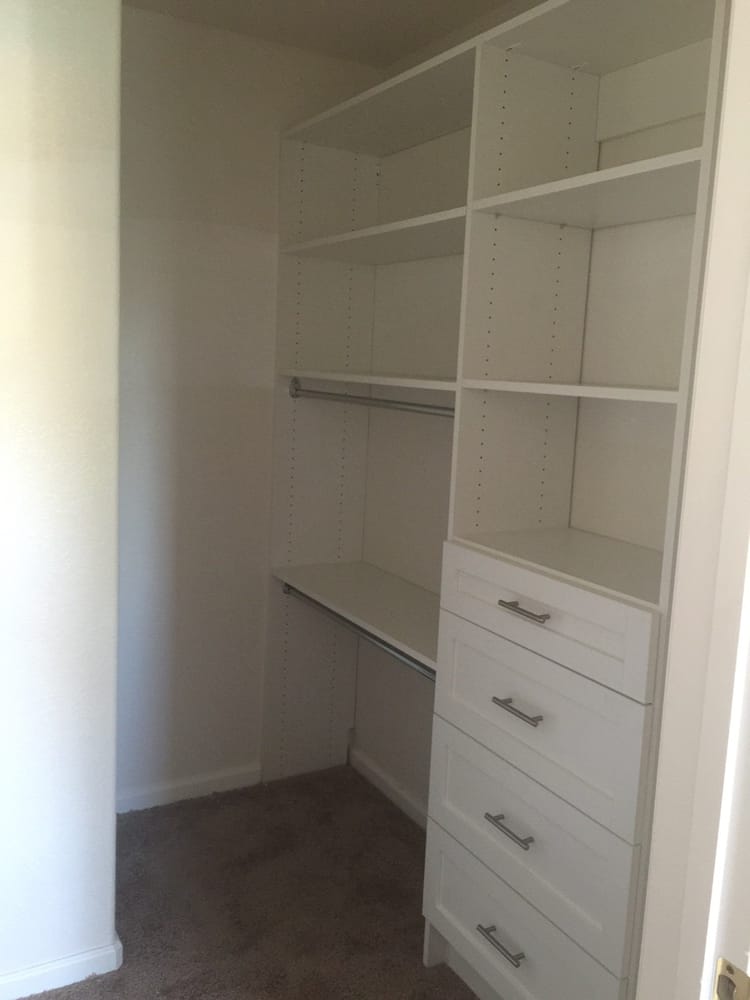 A walk in closet with white shelves and drawers in a bedroom.