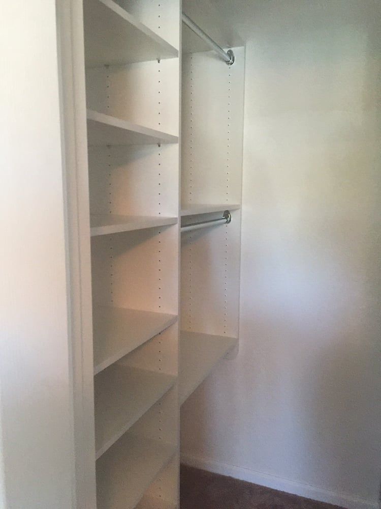 A walk in closet with white shelves and a hanging rail.
