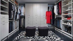 A walk in closet filled with lots of clothes and two ottomans.