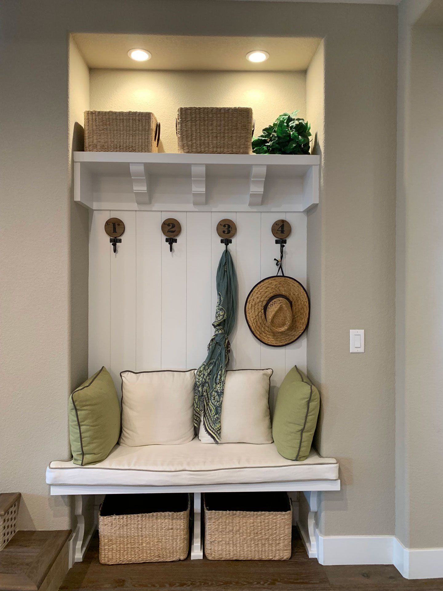 A bench with pillows and baskets in a hallway with a shelf above it.