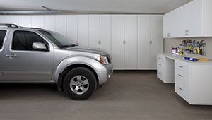 A silver suv is parked in a garage with white cabinets.
