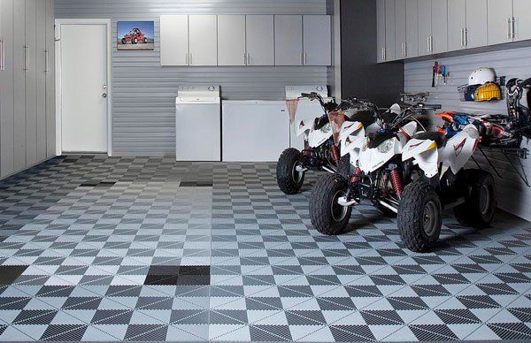 Two atvs are parked in a garage with a checkered floor.