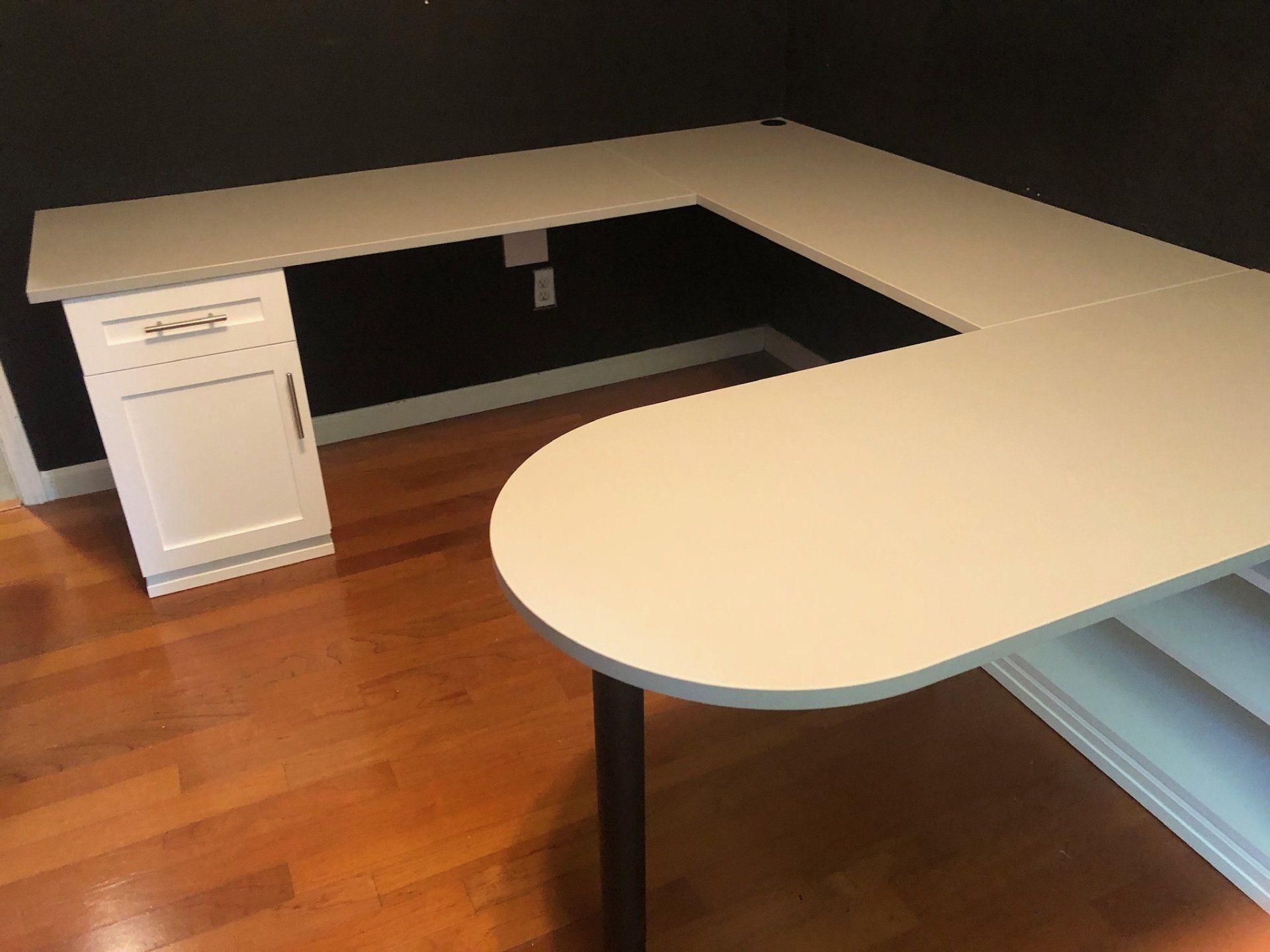 A white l shaped desk in a room with hardwood floors