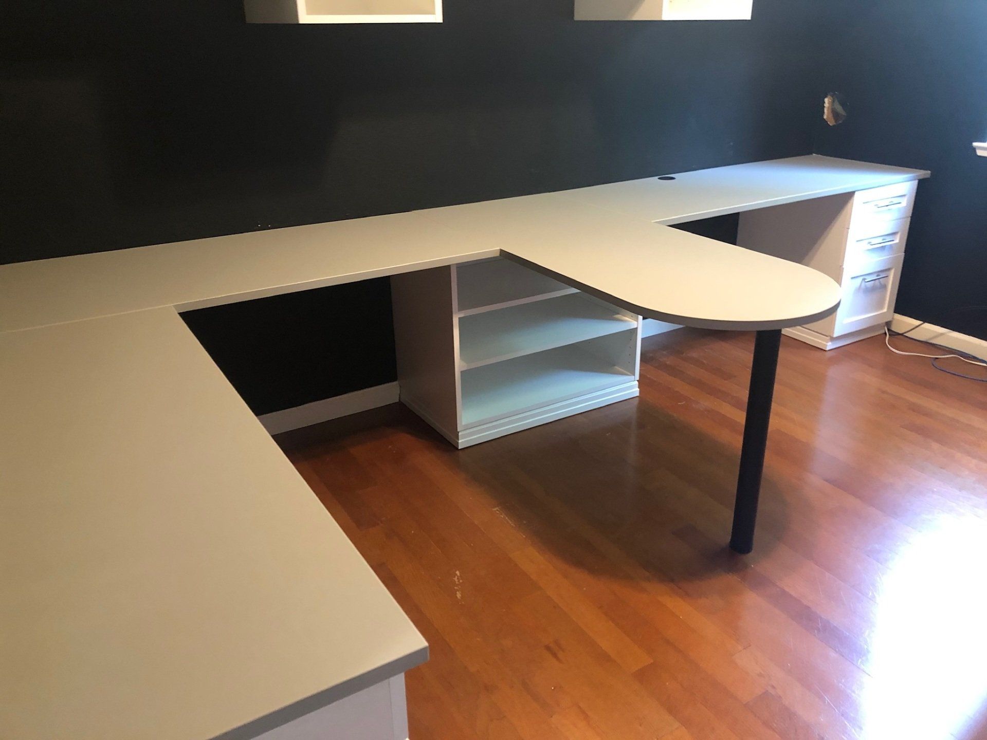 A white desk with a black leg is in a room with hardwood floors.