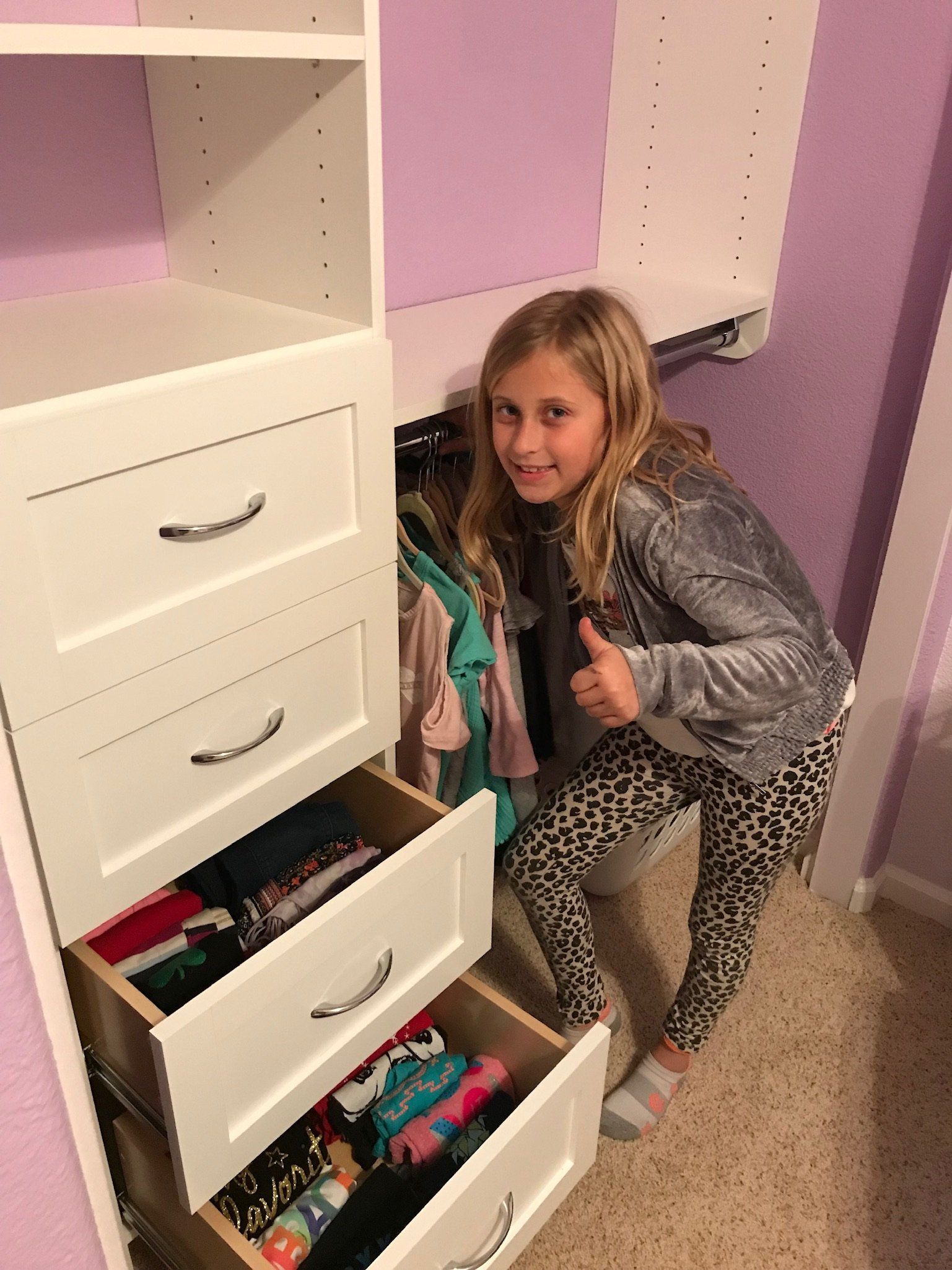 A little girl is standing in a closet giving a thumbs up