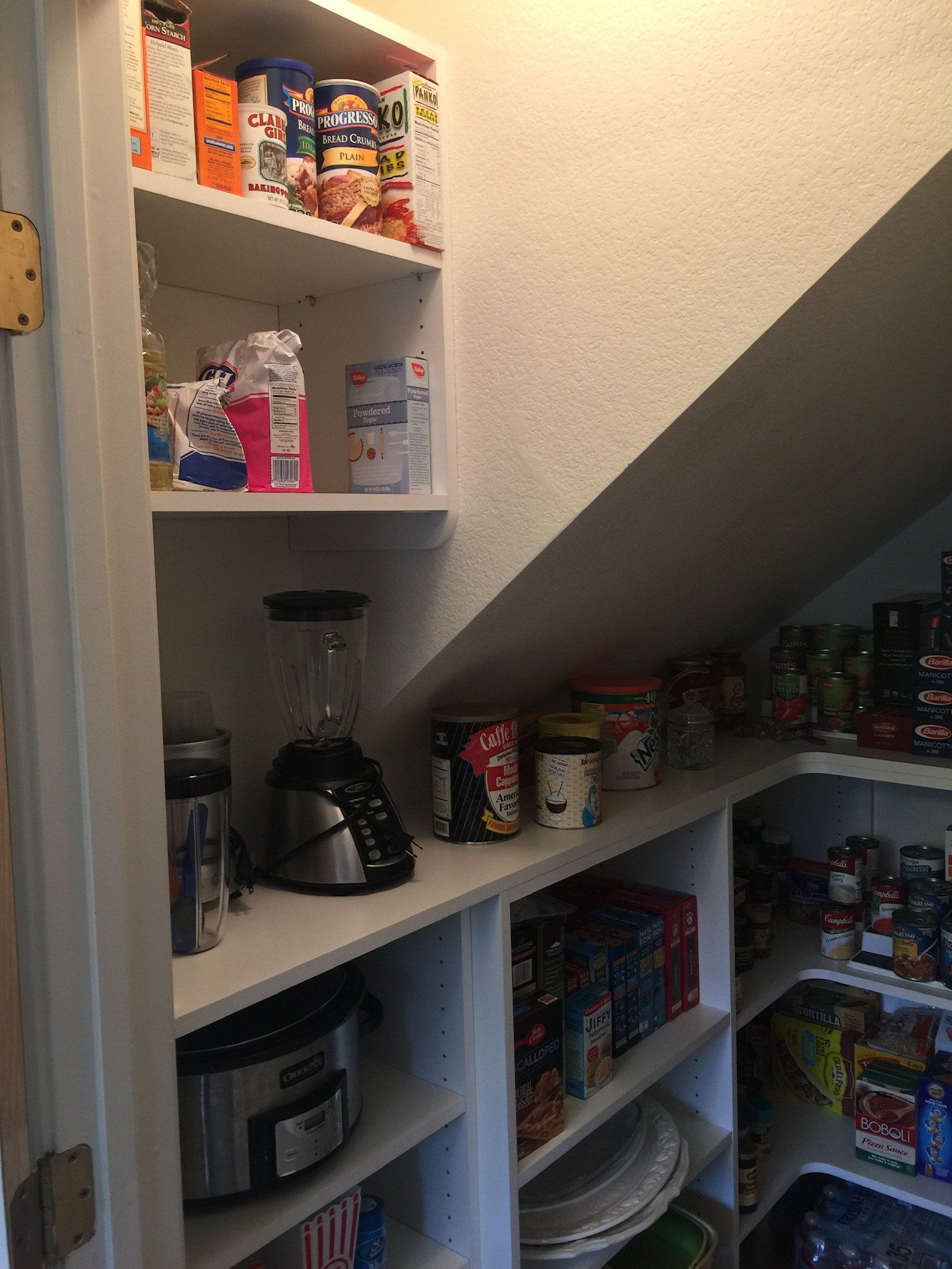 A pantry under a staircase filled with food and appliances.