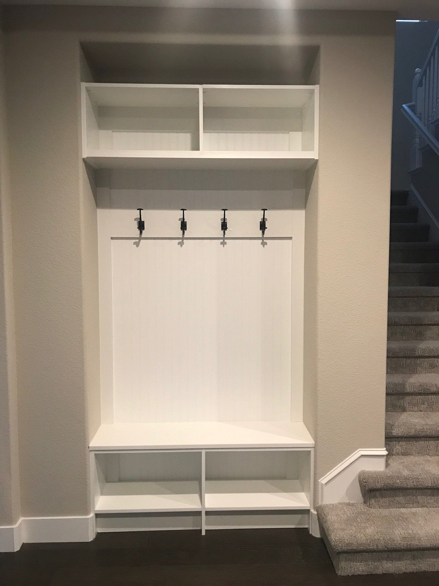 A hallway with stairs and a white shelf with hooks on the wall.