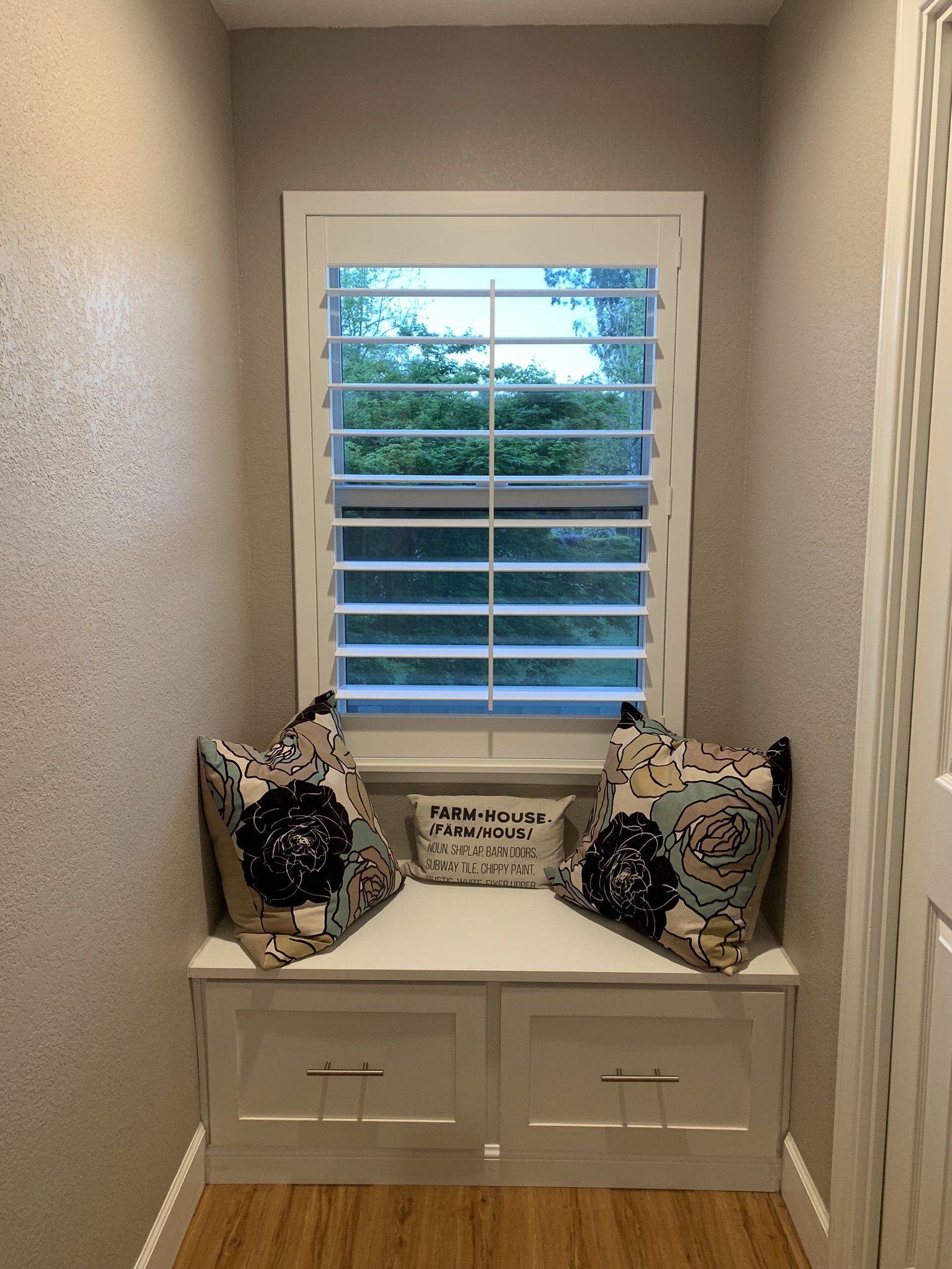 A corner of a room with a window seat and shutters.