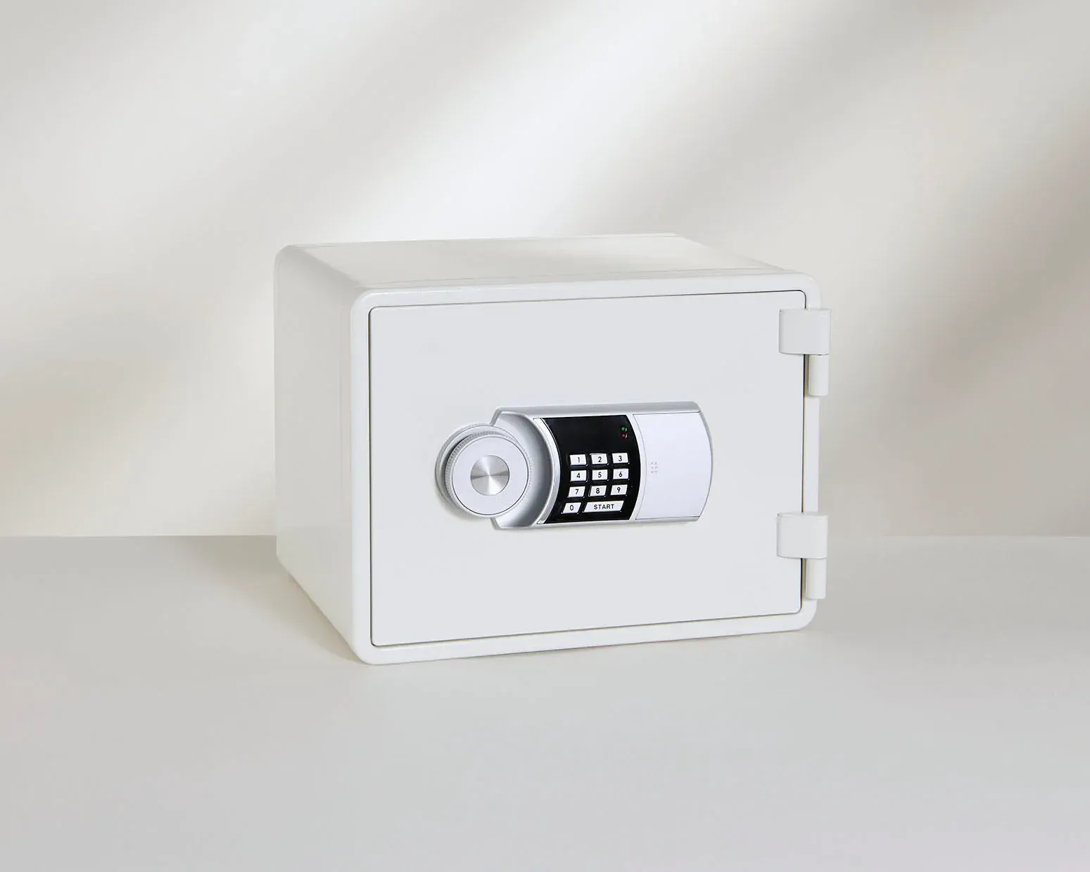 A white safe with a digital lock is sitting on a white table.