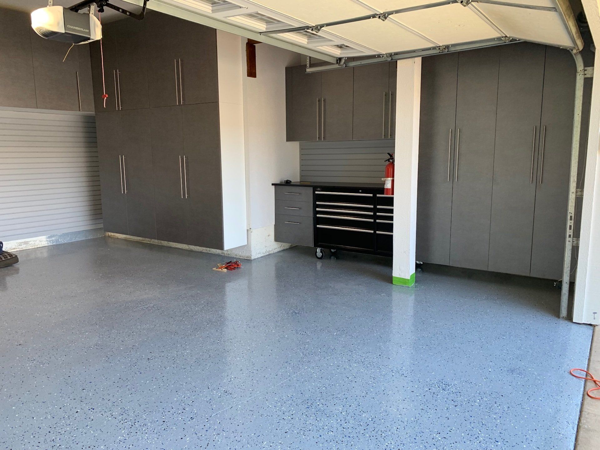 An empty garage with a garage door open and a fire extinguisher on the floor.