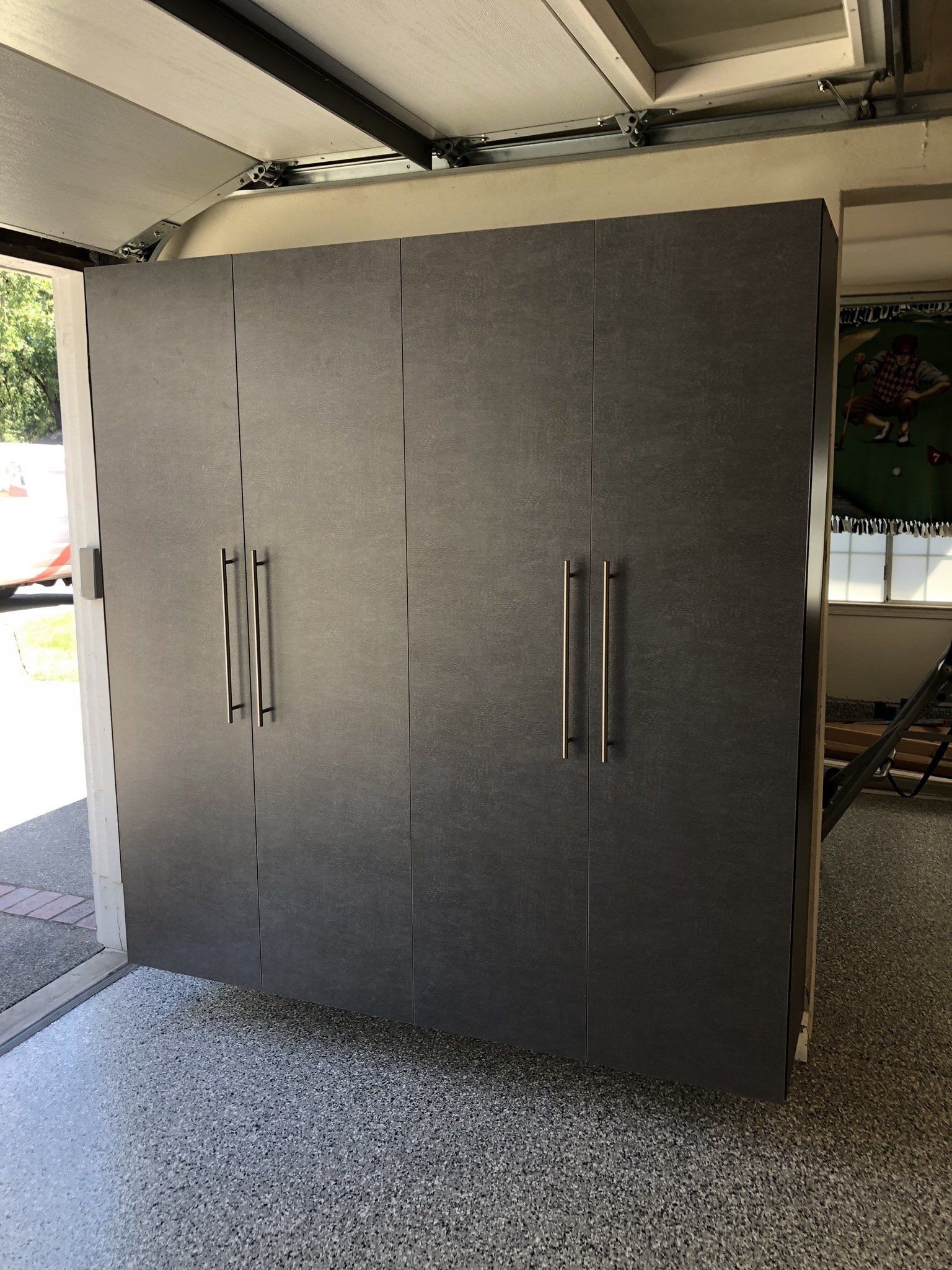 A large gray cabinet is sitting in a garage next to a window.