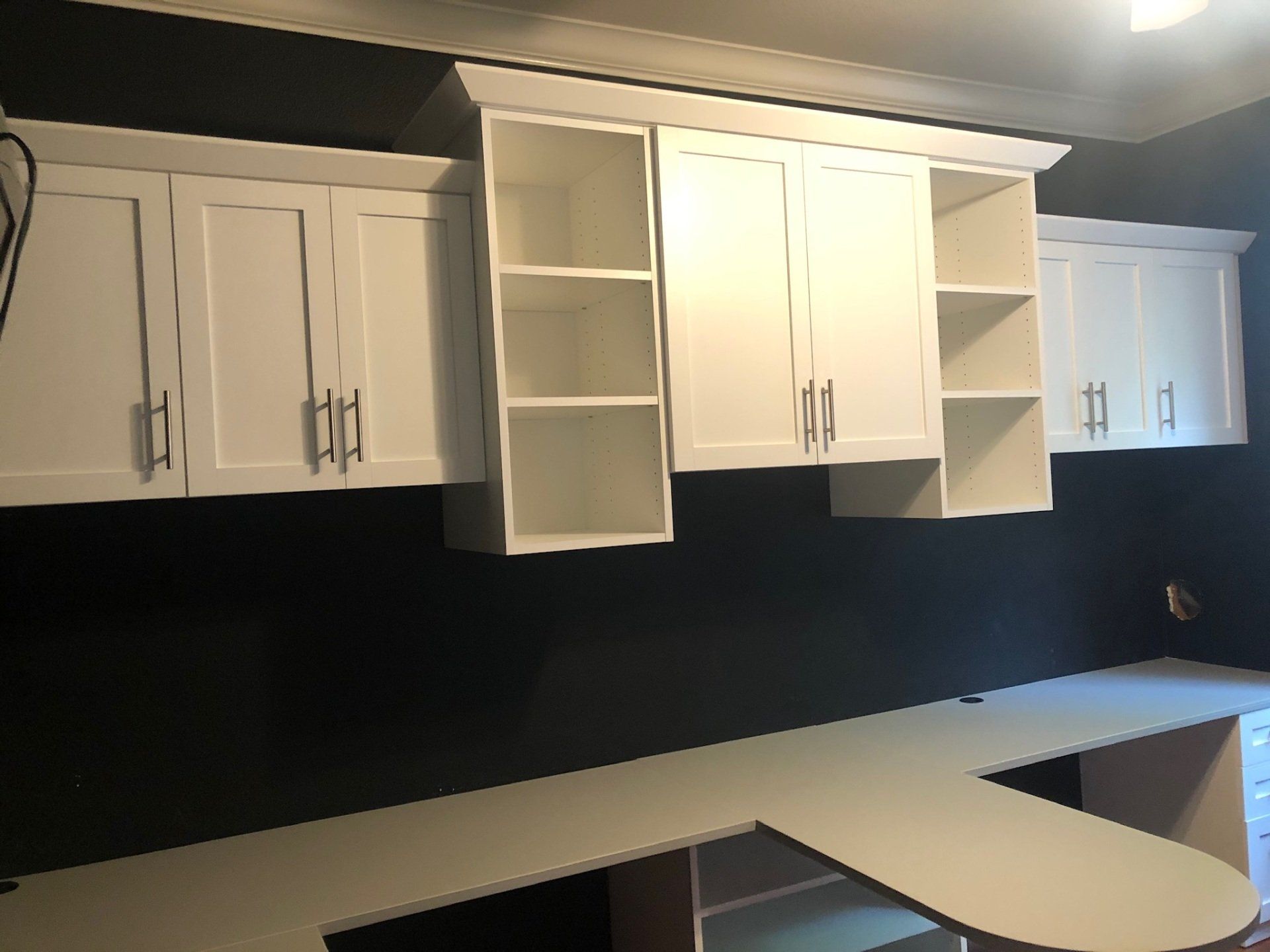 A kitchen with white cabinets and shelves and a desk.