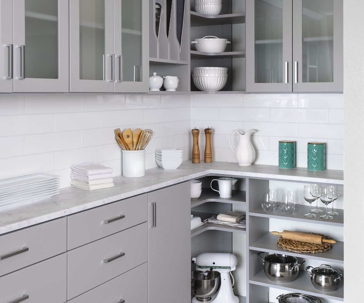 a kitchen with gray cabinets , white counter tops , and glass doors .