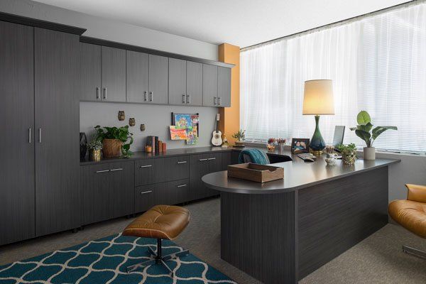 A home office with a desk , chair , lamp and cabinets.