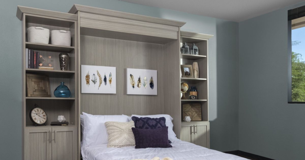 A light wood wall bed unit with integrated shelving and storage cabinets surrounding a made bed in a room with blue walls.