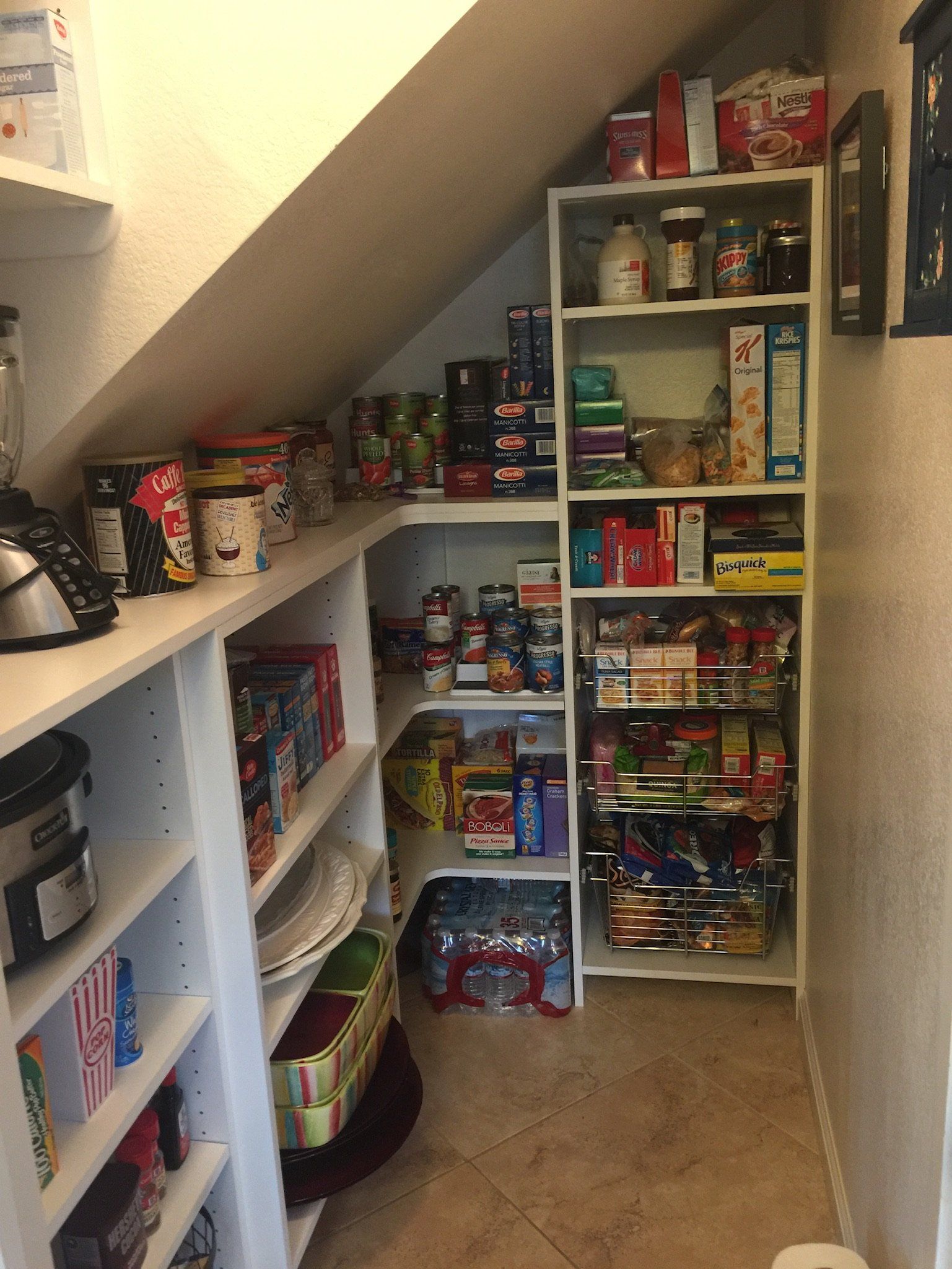 A pantry under a staircase filled with lots of food.