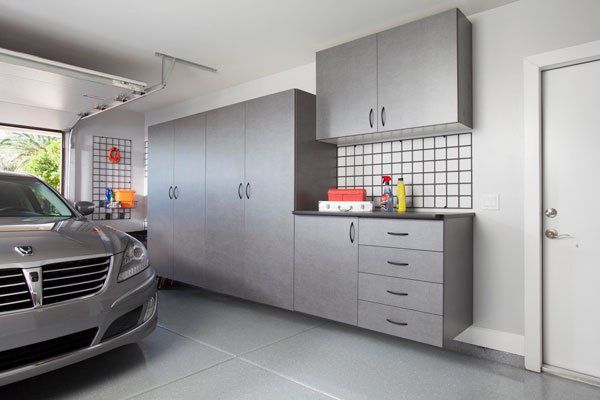 A car is parked in a garage with lots of cabinets and drawers.