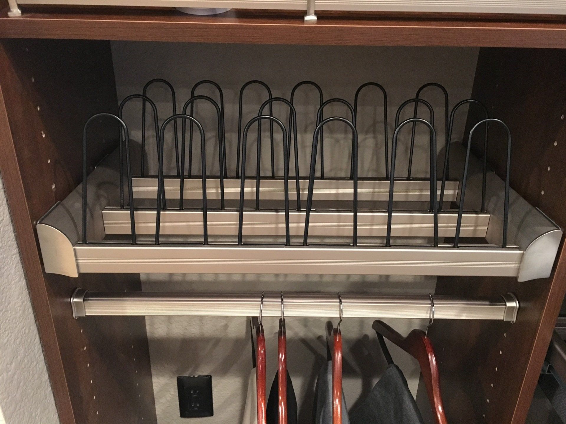 A shoe rack in a closet with clothes hanging on it