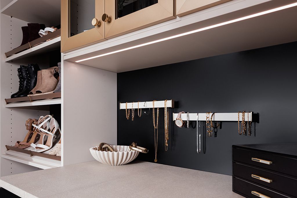 A closet with a jewelry rack and a bowl of jewelry on the counter.