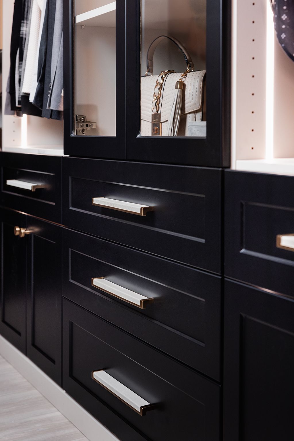 A walk in closet with black drawers and glass doors
