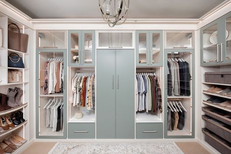 A walk-in closet with sage green cabinets, glass-front wardrobe sections, hanging clothes, and organized storage shelves.