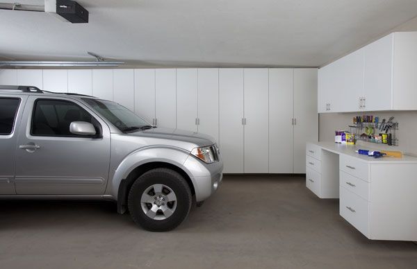 A silver suv is parked in a garage with white cabinets