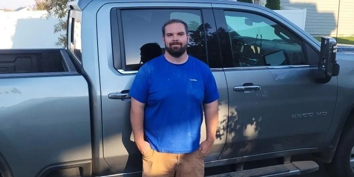A man in a blue shirt stands in front of a truck