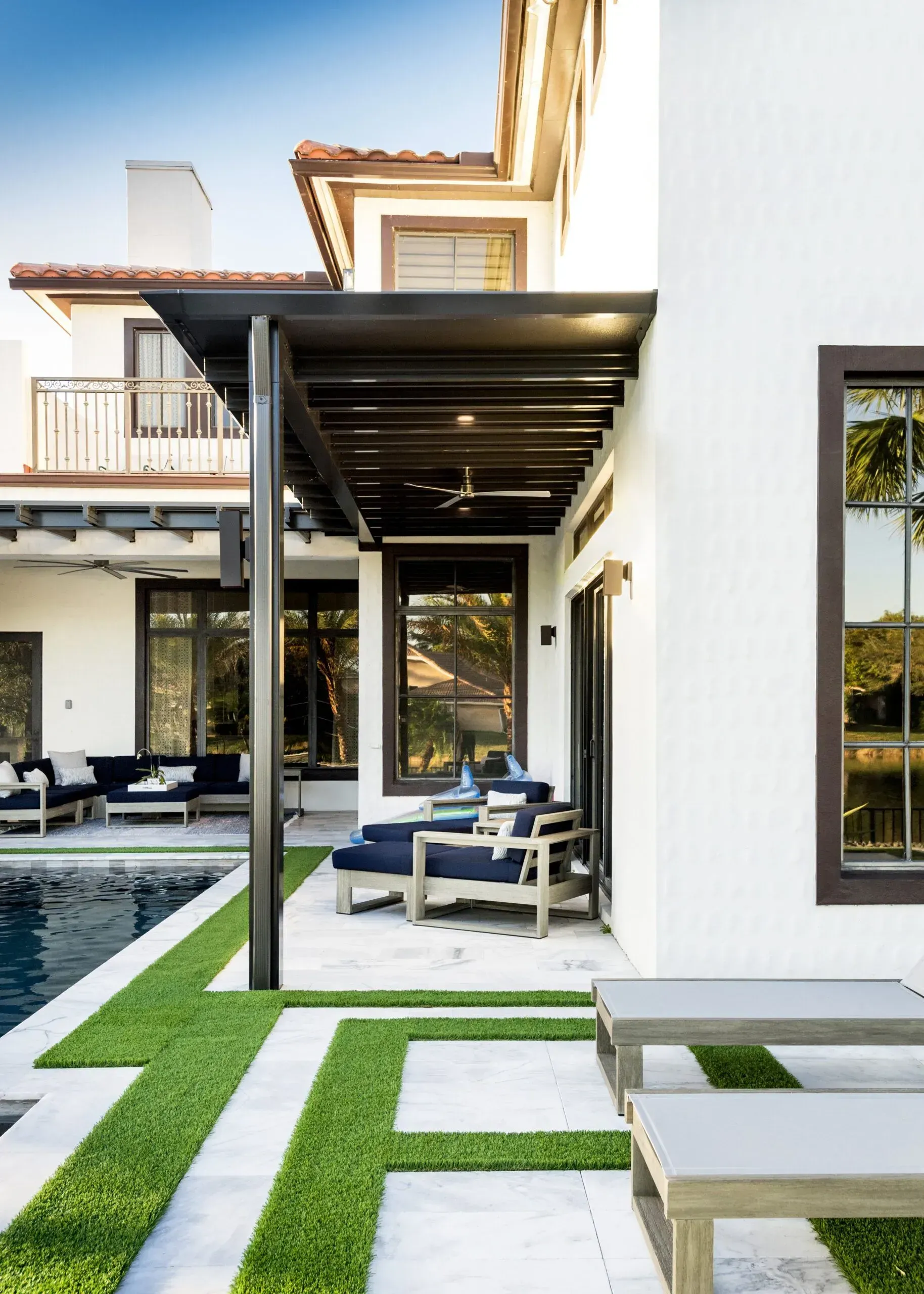 Modern home courtyard with white walls, black pergola, lounge chairs, and stepping-stone lawn.