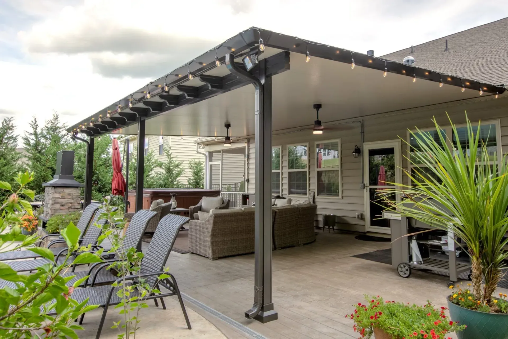 Covered patio with outdoor seating, string lights, and potted plants beside a house