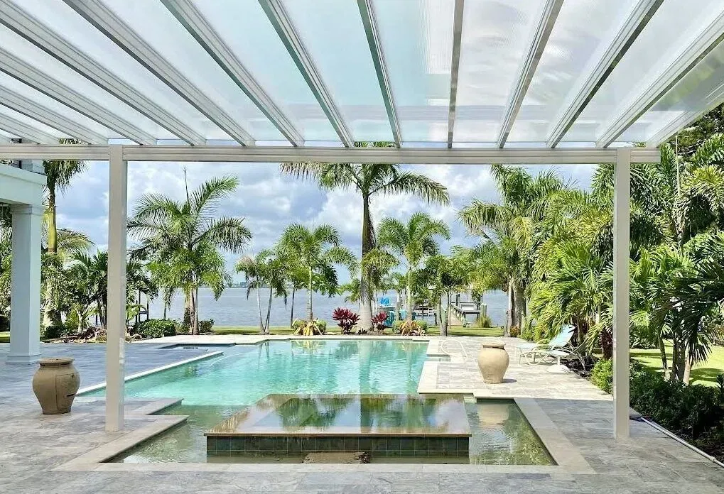 Modern patio overlooking a turquoise pool and tropical beach with palm trees and white pergola columns