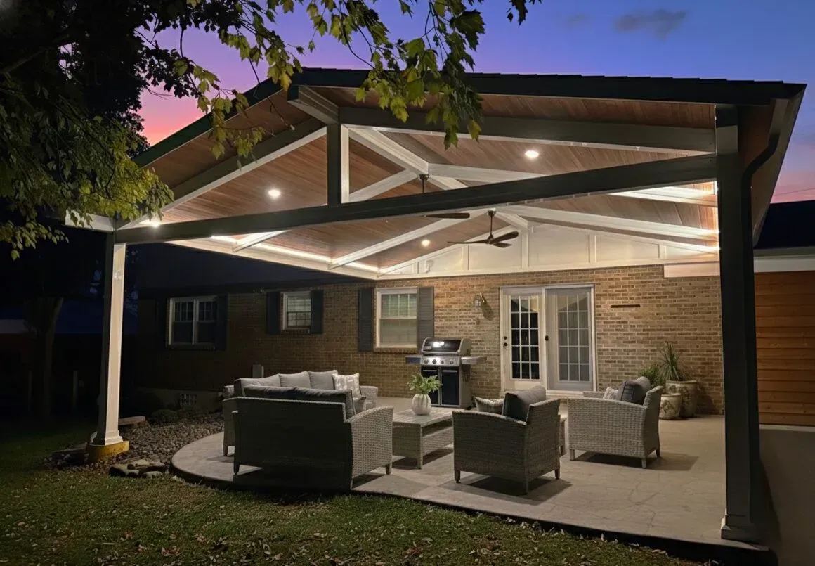 Covered patio with modern outdoor seating, grill, and warm string lights at dusk.