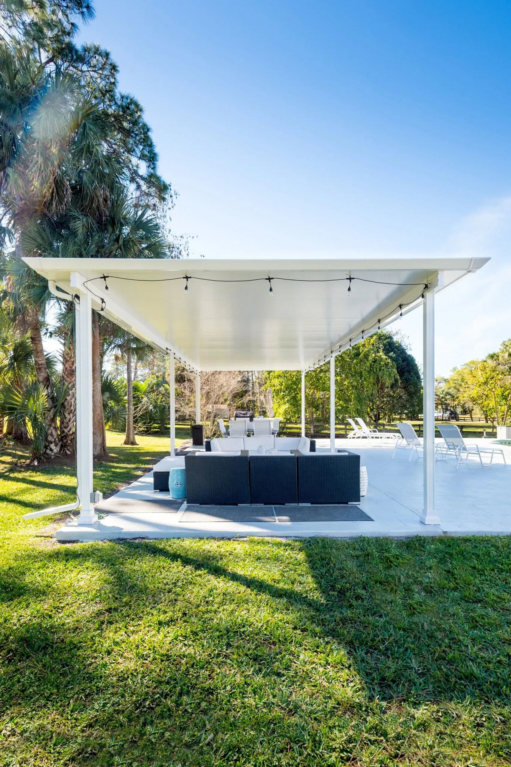 White outdoor pavilion with a stage-like platform in a sunny park, surrounded by grass and trees