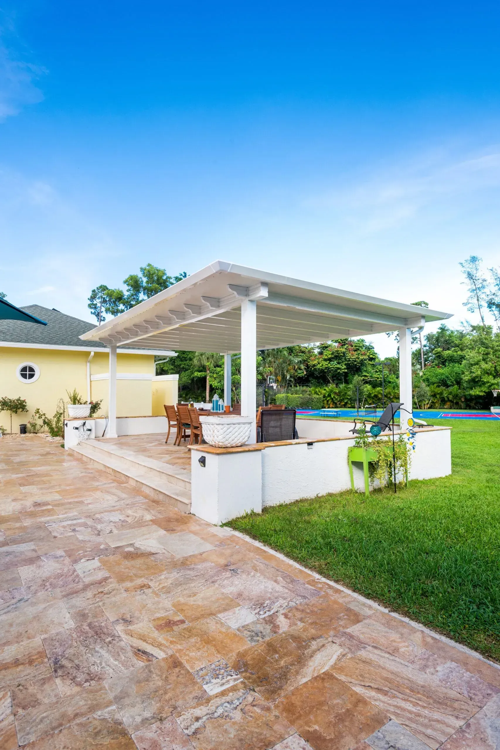 Outdoor patio with white pergola, stone walkway, and green lawn under a blue sky