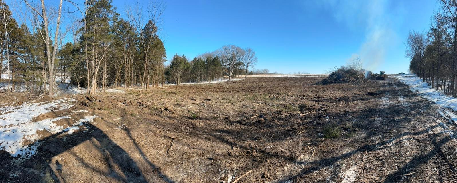 Woman in straw hat smiles, holding wine glass near a lake.