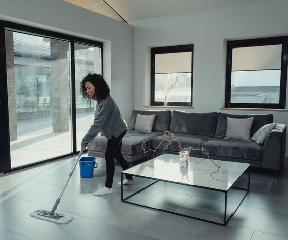 A woman is cleaning the floor in a living room with a mop.