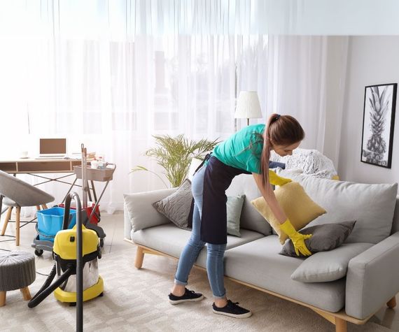 A woman is cleaning a couch in a living room.