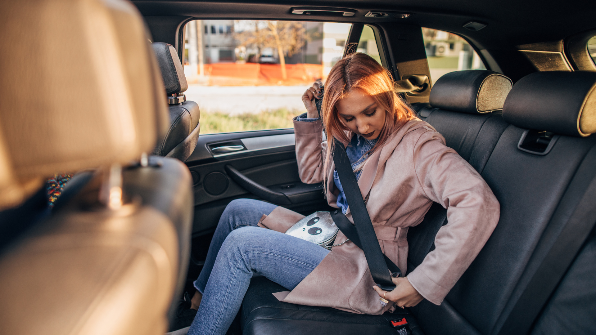 Woman in backseat of car fastening seatbelt.