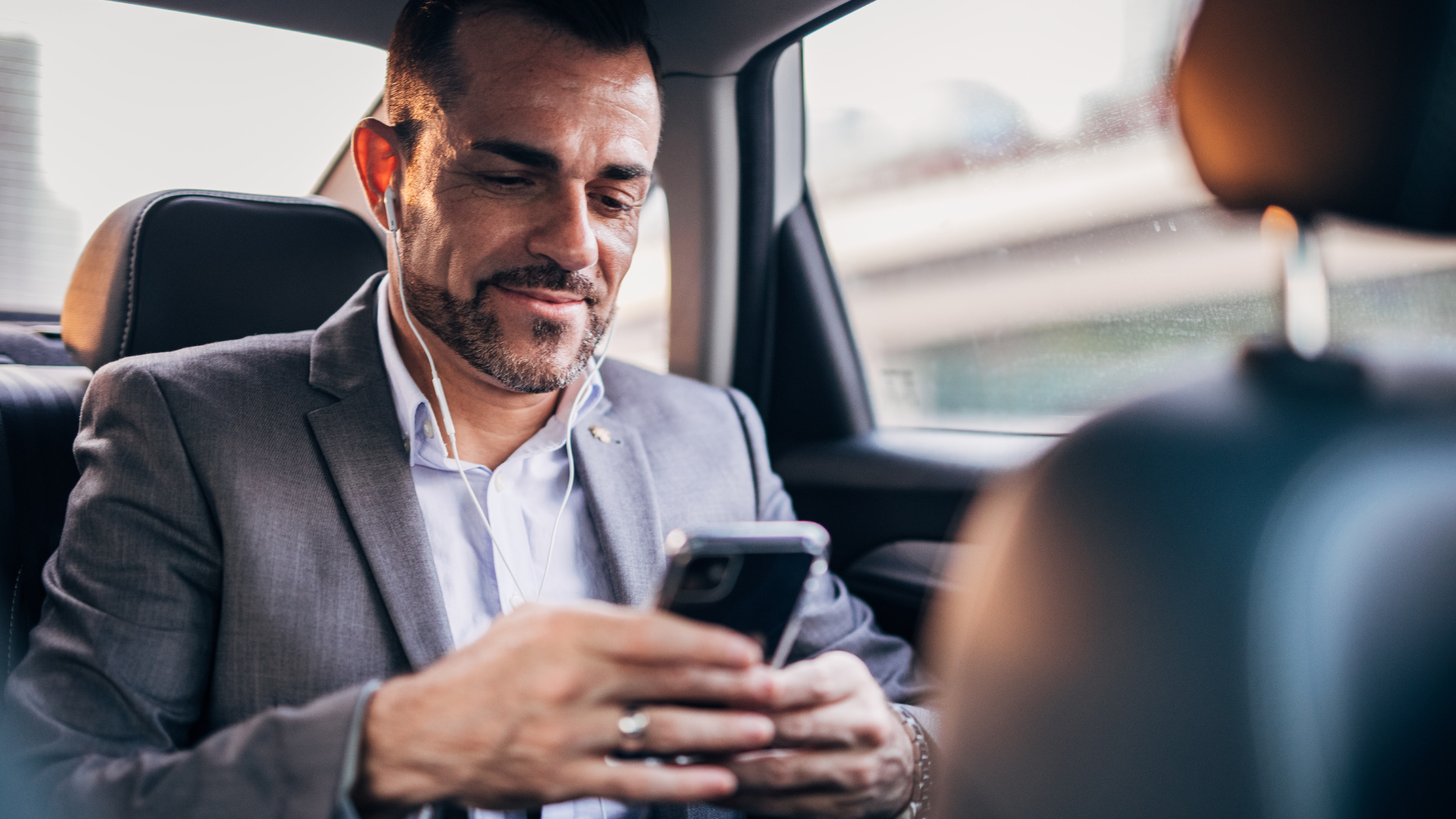 Man in a suit using a smartphone in the backseat of a car.
