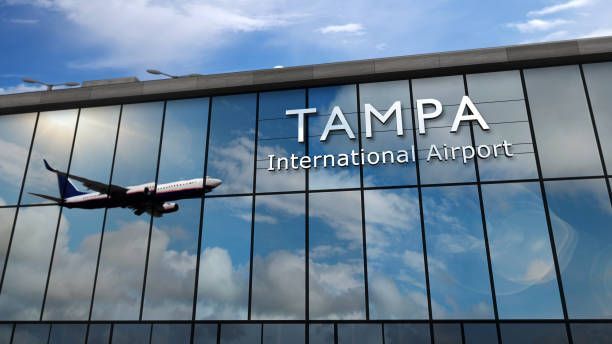 Tampa International Airport facade with a plane taking off, reflected in the glass. Blue sky and clouds.