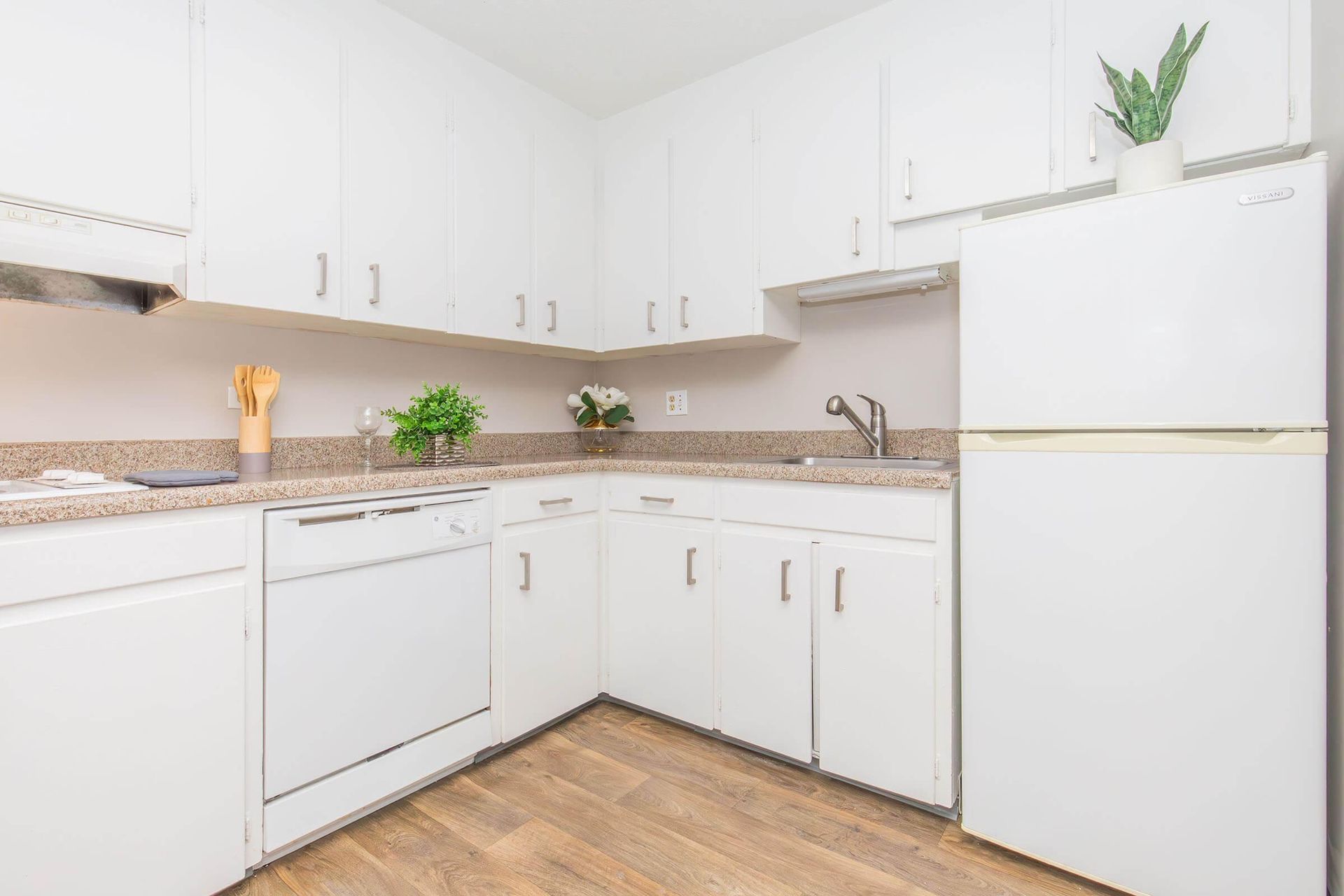 White kitchen with cabinets, appliances, light-colored countertops, and wood flooring.