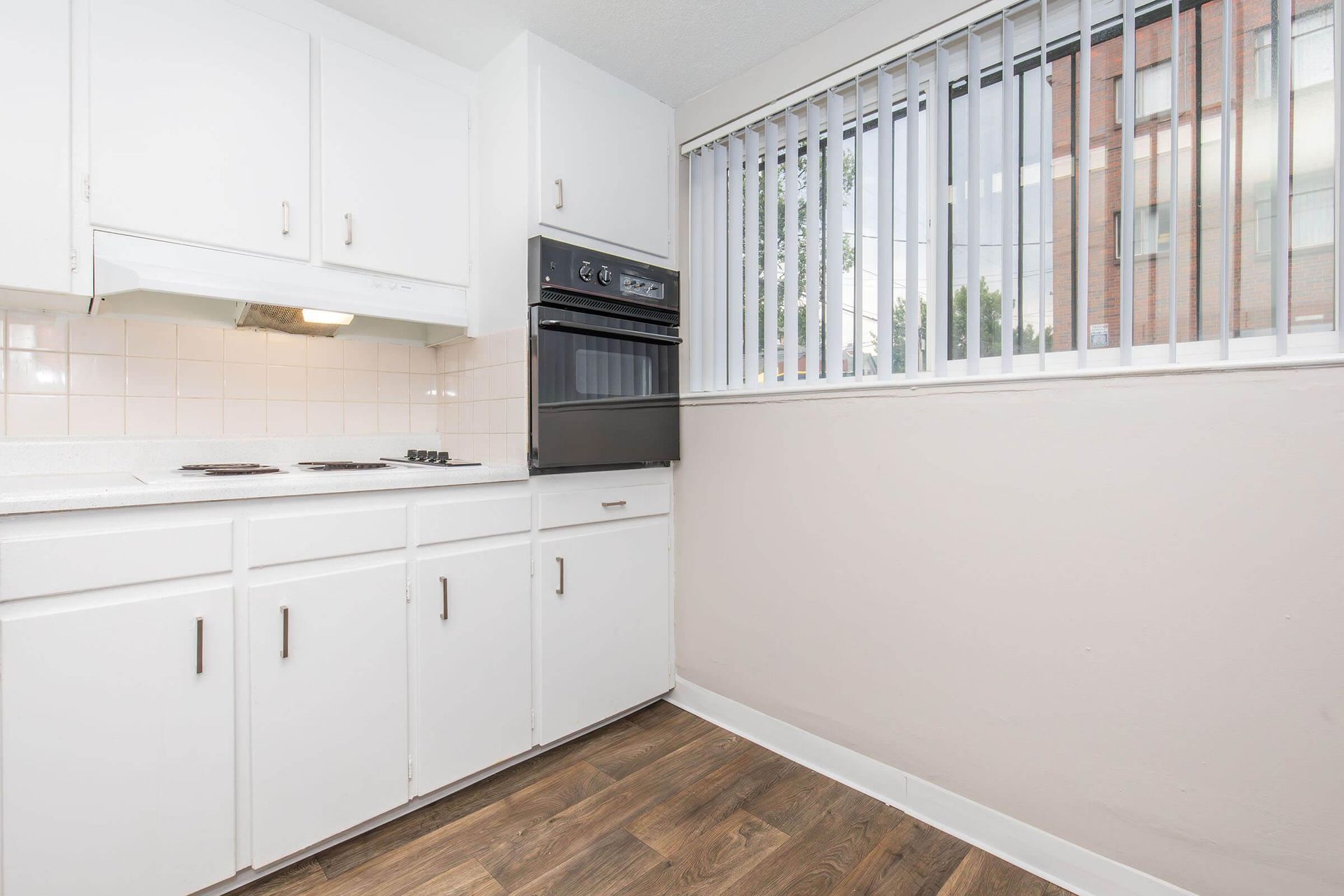 White kitchen with cabinets, oven, stovetop, and window with blinds.