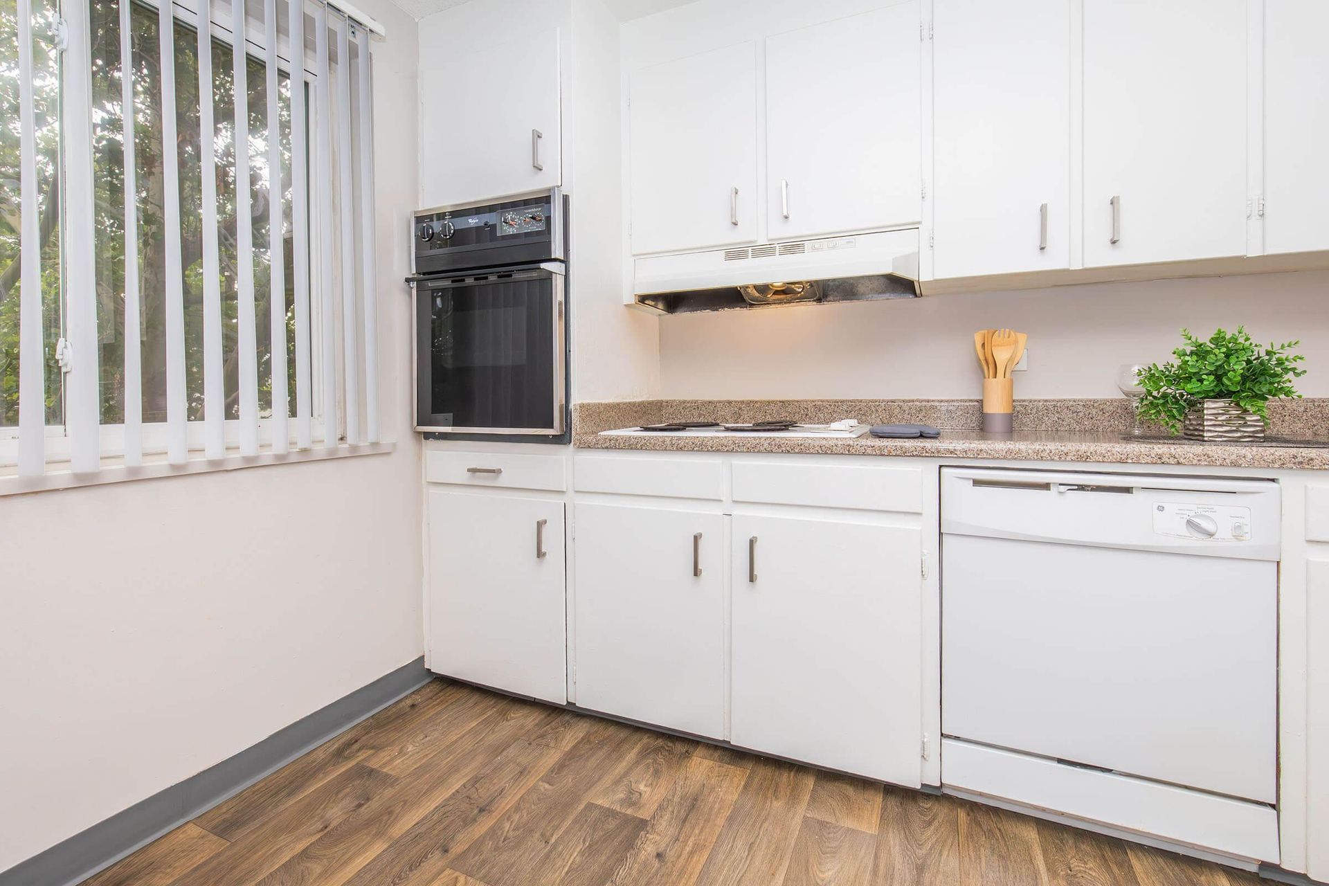 White kitchen with cabinets, oven, stove, and dishwasher; window with blinds.