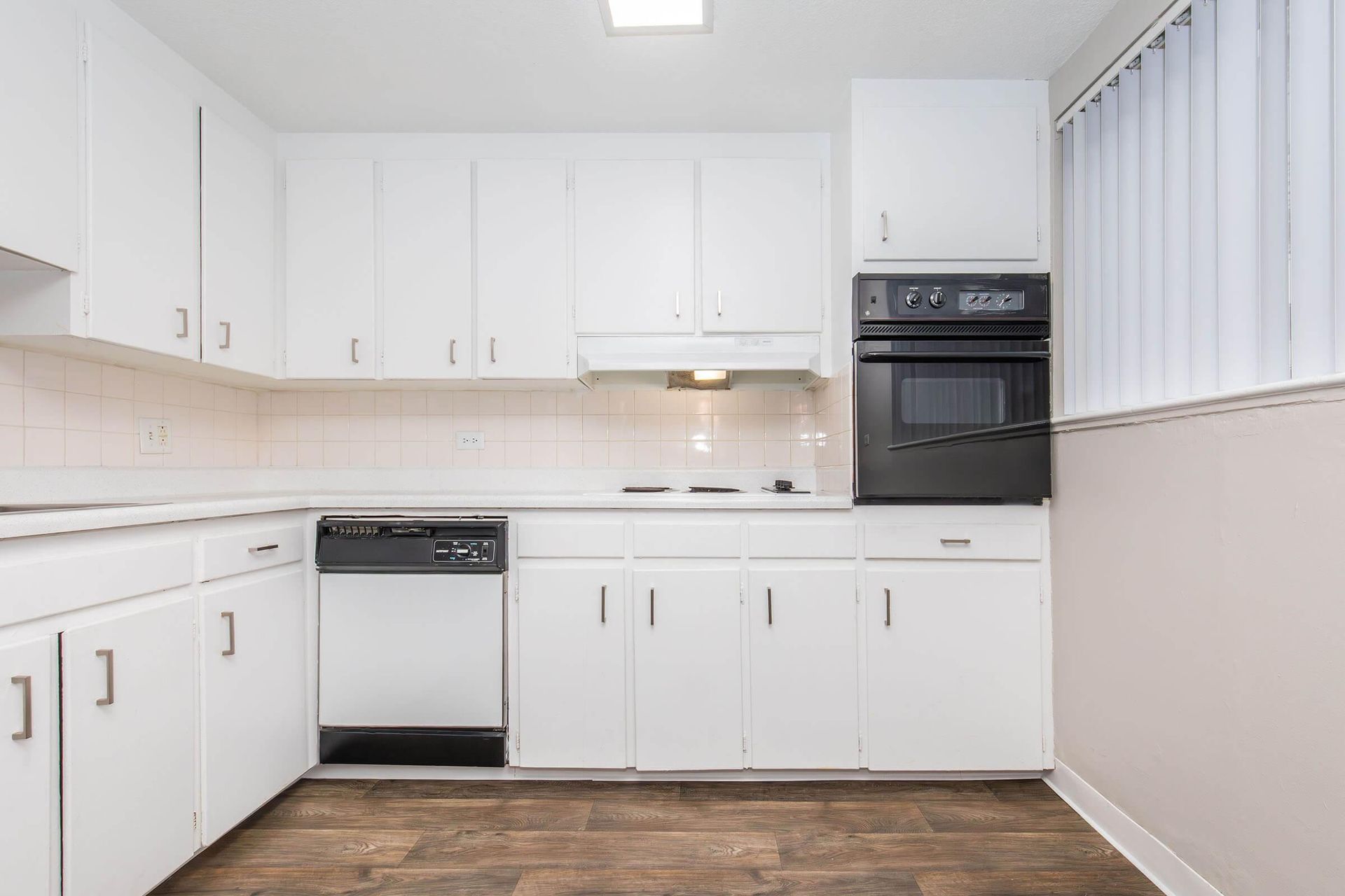 White kitchen with cabinets, appliances, and a window with blinds.
