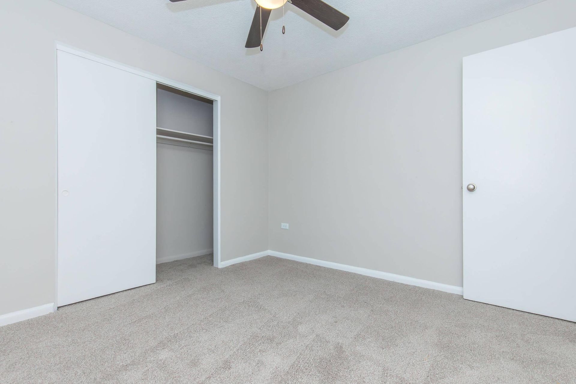 Empty bedroom with closet, two doors, ceiling fan, and gray carpet.