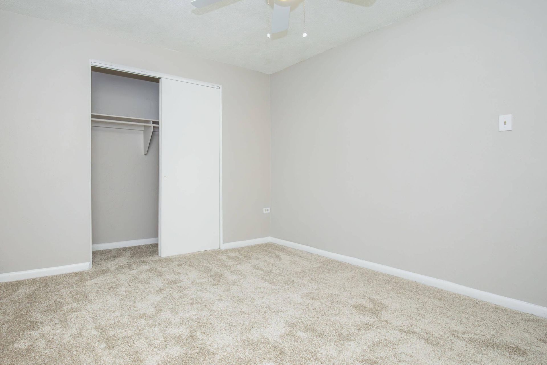 Empty bedroom with white walls, carpeted floor, closet, and ceiling fan.