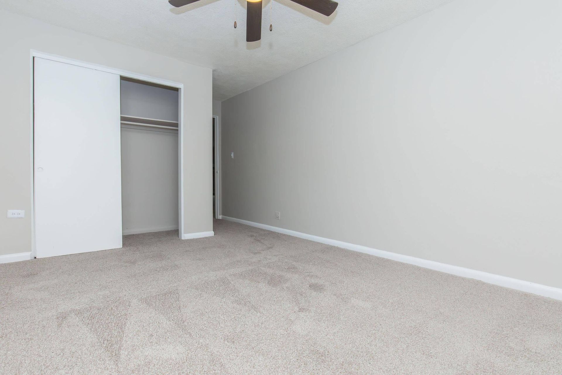 Empty bedroom with beige carpet, sliding closet doors, and a ceiling fan.