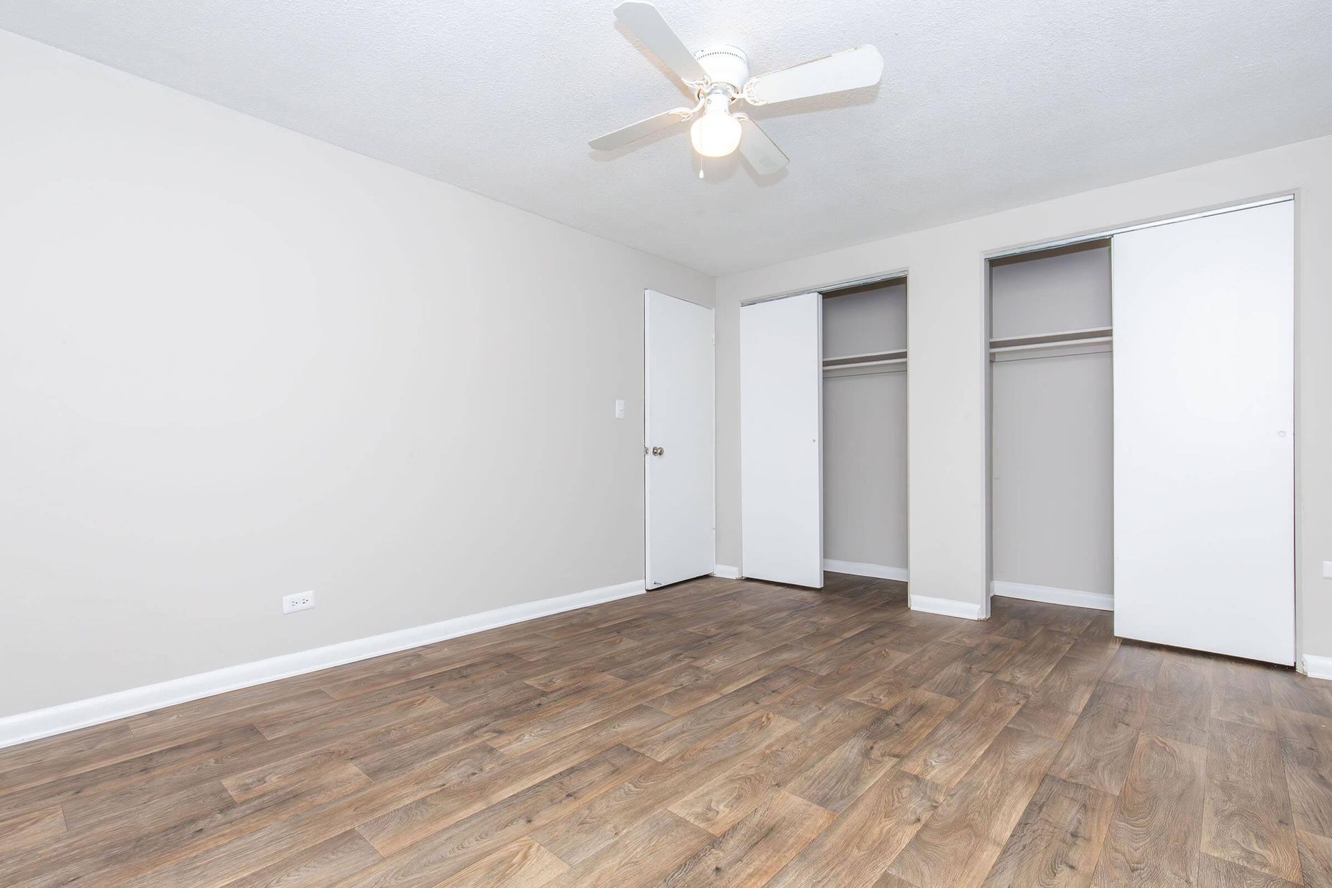 Empty bedroom with wood-look flooring, two closets, and a ceiling fan.