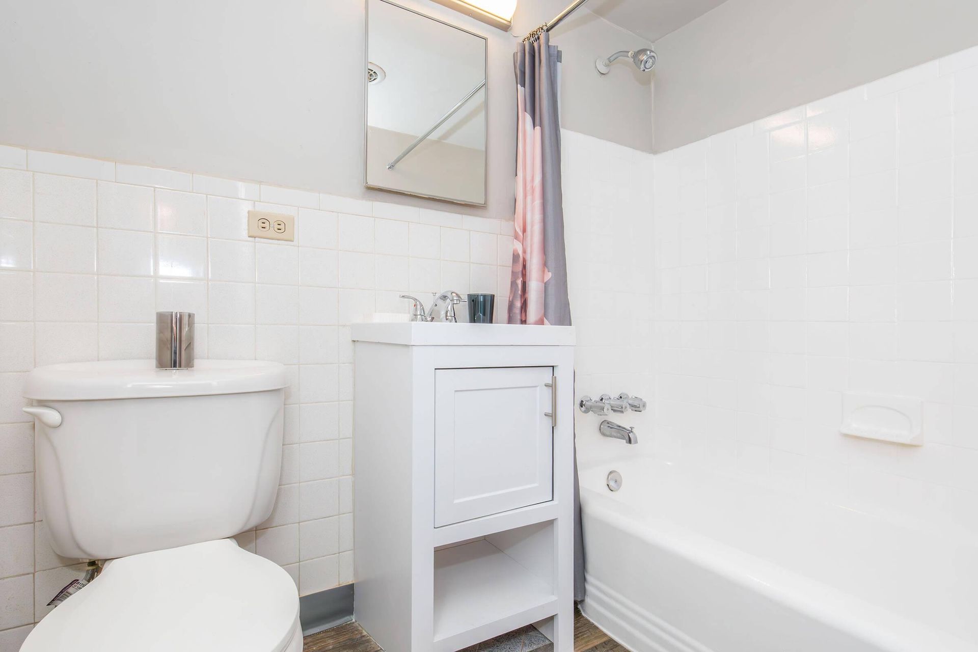 White bathroom with toilet, sink, mirror, and shower/tub.